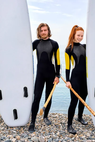 Joven pareja positiva se divierten de pie en la playa, preparándose para el stand up paddleboard —  Fotos de Stock