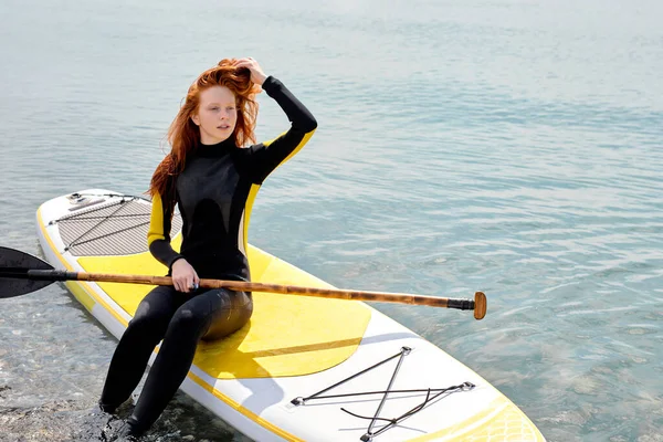 Stand up paddle board mujer paddleboarding en la playa, sentado en el paddleboard —  Fotos de Stock