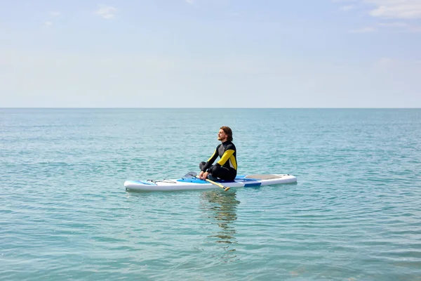 Widok z boku portret spokojnego brodatego faceta siedzącego na paddleboard medytującego po supsurfingu — Zdjęcie stockowe