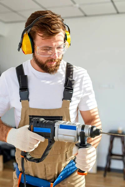 Confident caucasian male using electric drill making hole on wall, decorating