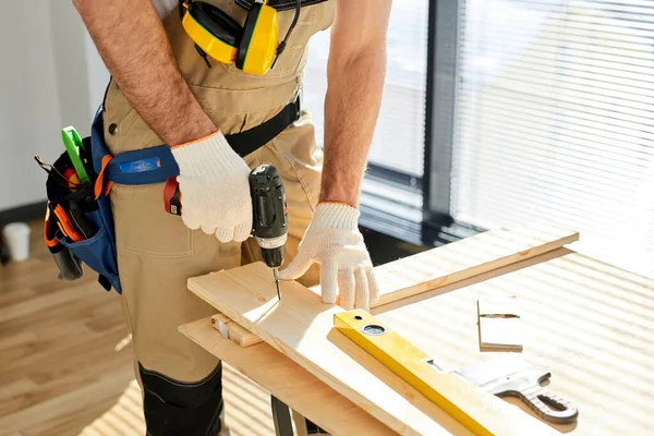 Trabajador de la madera taladra agujero con un taladro eléctrico en tablero de madera. Foto de cerca de las manos con taladro —  Fotos de Stock