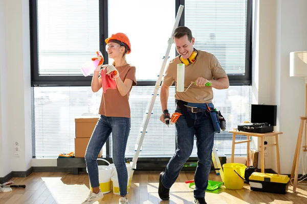 Emocionada pareja joven sosteniendo herramientas y bailando durante la reparación de la casa —  Fotos de Stock