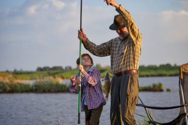 Beyaz ırktan çok nesilli bir aile birlikte balık tutuyor. Çocuk büyükbabasıyla açık havada balık tutuyor.