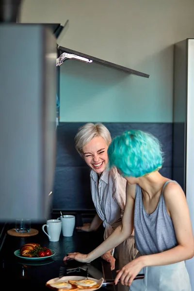 Emocionado alegres mujeres lesbianas pareja divertirse en la cocina mientras cocina el desayuno —  Fotos de Stock