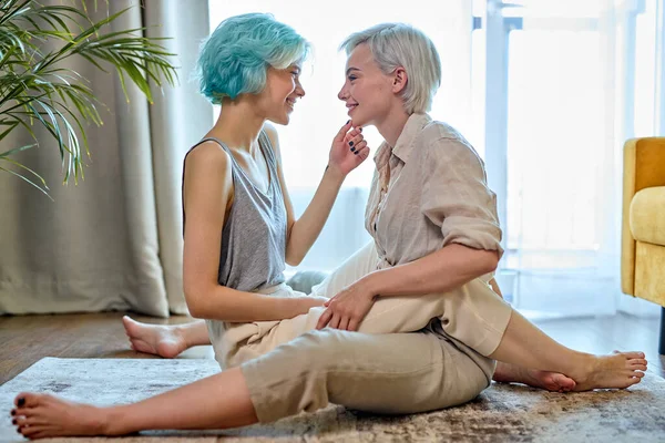 Lesbian couple hugging and kissing while sitting on floor at home in cozy room, side view — Stock Photo, Image