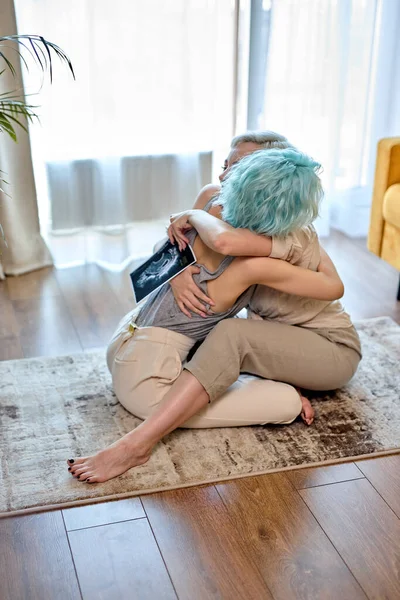 레즈비언 부부는 거실 바닥에 같이 앉아 키스하고 껴안고 있습니다. 임신 소식 이후에요. — 스톡 사진