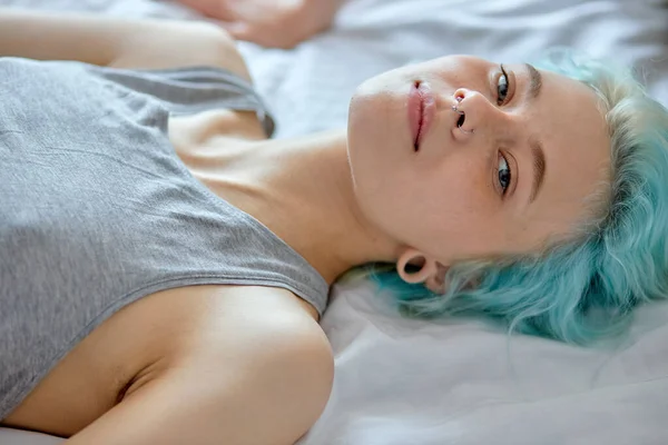 Calm female with unusual beauty and green blue hair style lying on bed relaxing — Stock Fotó