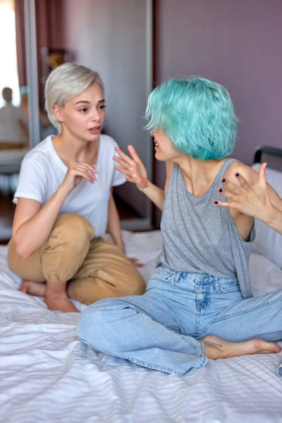 Two female friends or lesbians sitting on bed, arguing with each other. Friendship, quarrel