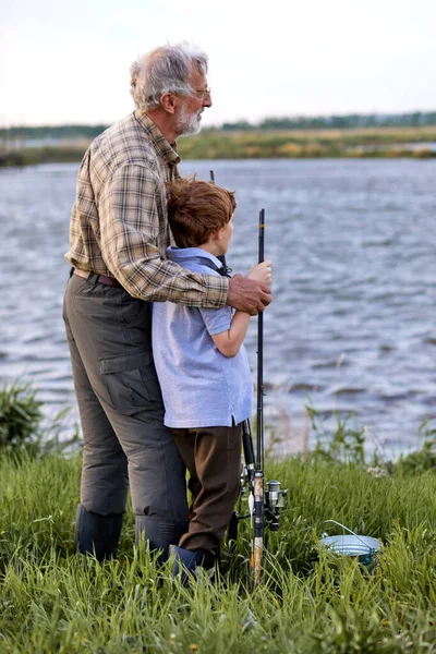 Caucasian family fishing together from riverside in the evening, grandfather and grandson — Fotografia de Stock