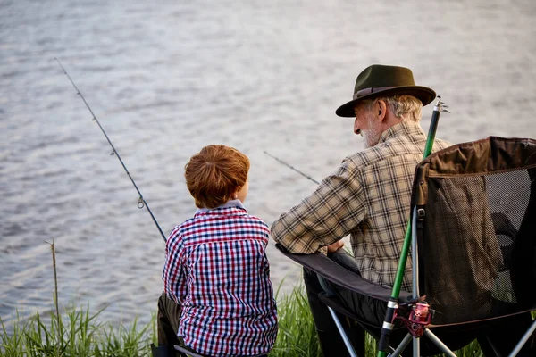 Caucasian senior fisherman teaching cute grandkids fishing on lake in nature — Fotografia de Stock