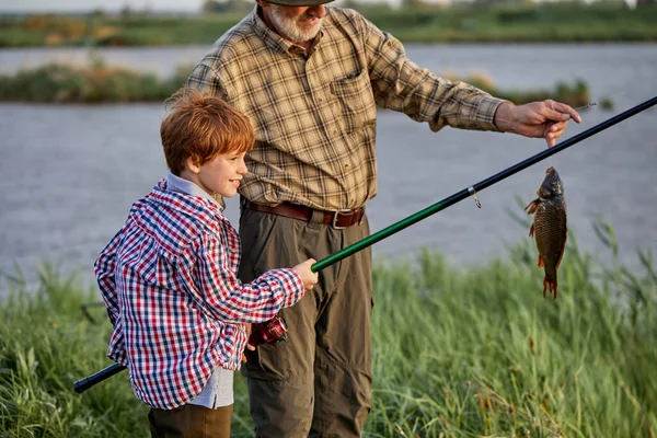 Niño pescando en el lago con el abuelo. cath un pez con caña de pescar, feliz y emocionado — Foto de Stock