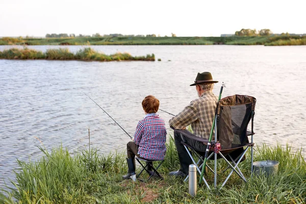 Back view portrait of adult man and teenage boy sitting together on lake fishing with rods — Fotografia de Stock