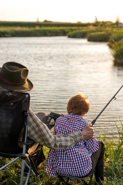 Rear view senior man and child boy engaged in fishing together, on countryside lake — Fotografia de Stock
