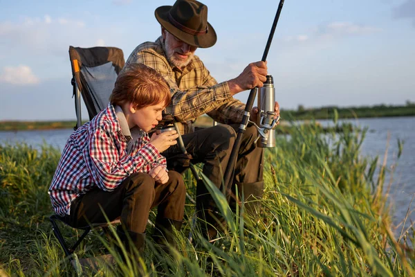 Happy senior man and child boy engaged in fishing together, on countryside lake — Fotografia de Stock