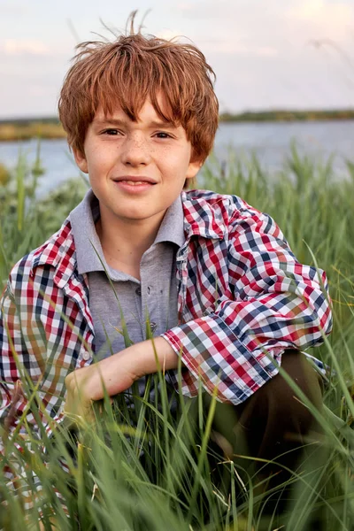 Schattig roodharige tiener jongen in casual geruite shirt kijken naar camera terwijl zitten in veld — Stockfoto