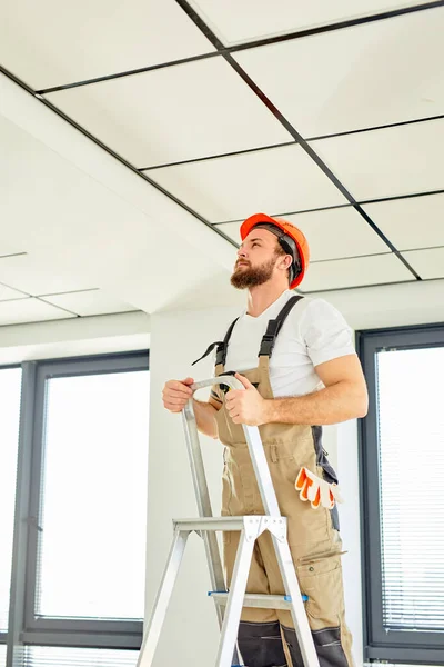 Electricista escalando escalera haciendo renovación de la casa. trabajador de la construcción en casco de seguridad —  Fotos de Stock