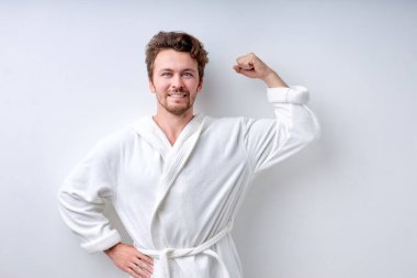 Genç sakallı adam vücut geliştirme çalışmasından sonra bornozla kaslarını gösteriyor.