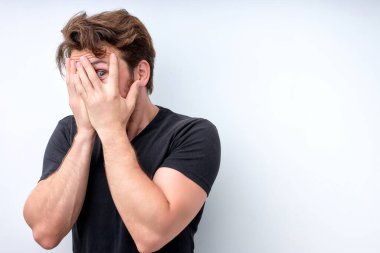 Stresli ve korkmuş genç çekici erkek yüzünü kapatıyor ve tek gözüyle kameraya bakıyor.