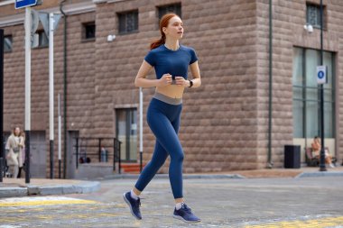 Şehirde koşan güzel bayan, yolun karşısına geç. Kırmızılı kadın spor giyim bölümünün yan görüntüsü
