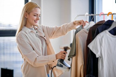 Sıcak buhar. Tişörtünü ütülerken elinde elektrikli buharlı gemi tutan hoş beyaz bir kadın.