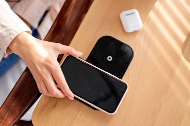 Kesilmiş kadın cep telefonunu kablosuz şarj cihazına bağlıyor. Boşluğu kopyala