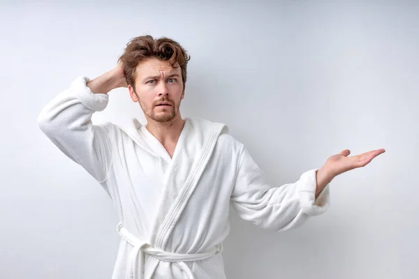 Young bearded man at a loss, misunderstanding guy in bathrobe isolated on white — Fotografia de Stock