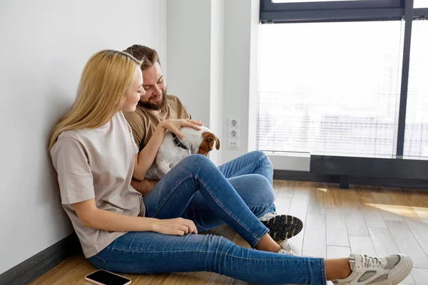 Positiva pareja caucásica familia sentarse en el suelo jugando con el perro mascota, divertirse, disfrutar — Foto de Stock