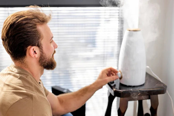 Молодой бородатый мужчина включить очиститель в комнате, в умном доме, с видом на сторону портрет — стоковое фото