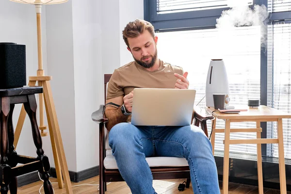 Male work on laptop in room with portable speaker, air purifier, in smart house alone — Zdjęcie stockowe