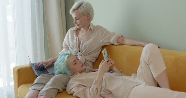 Lesbiska damer hemma, liggande på soffan, arbetar på laptop och surfar på nätet — Stockvideo