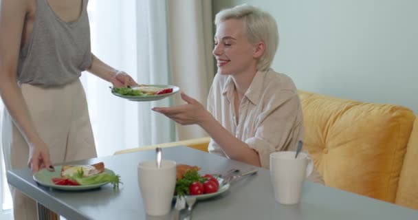 Όμορφη γυναίκα με κοντά μαλλιά κάθεται πίσω από το τραπέζι περιμένοντας για πρωινό από λεσβία φίλη — Αρχείο Βίντεο