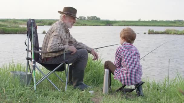 Abuelo y nieto durante la pesca en el río. Sentarse juntos en el campo con caña de pescar — Vídeos de Stock