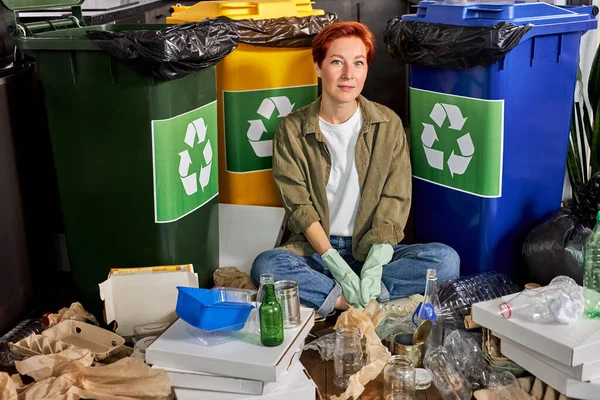 Rödhårig kvinna bland sopor, bland olika avfallsprodukter: glasbehållare, returpapper — Stockfoto