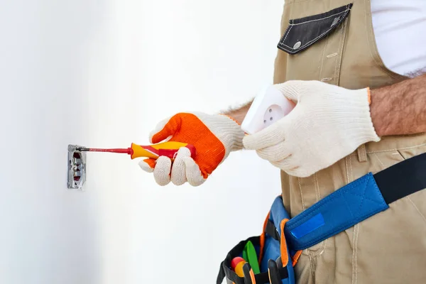 Mão de pessoas cortadas instalando soquete na parede em casa, reparador em macacões usando ferramentas — Fotografia de Stock