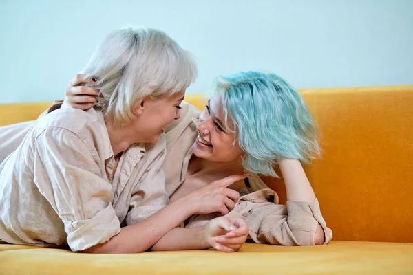 Очаровательная пара лесбиянок отдыхает дома, обнимаясь на диване в уютной комнате — стоковое фото