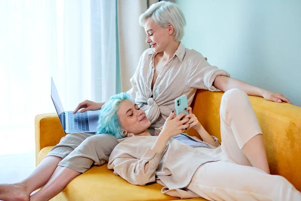 LGBT couple lesbien meilleures copines se reposer à la maison sur le canapé, avec ordinateur portable et smartphone — Photo