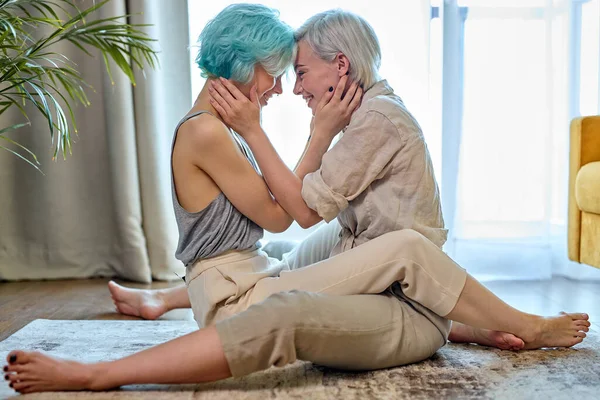 Lesbijki para przytulanie i całowanie siedząc na podłodze w domu w przytulnym pokoju, widok z boku — Zdjęcie stockowe