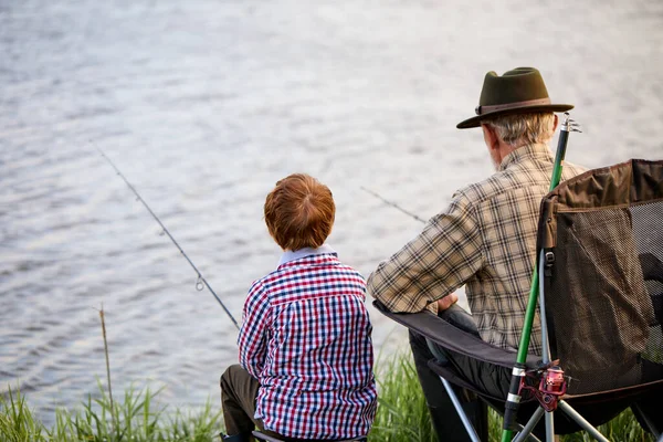 Tillbaka visa porträtt av kärleksfull farfar och pojke fiske vid sjön tillsammans, i naturen — Stockfoto