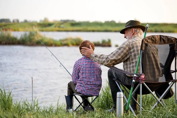 Vista posterior retrato de buen abuelo y niño pescando junto al lago juntos, en la naturaleza — Foto de Stock