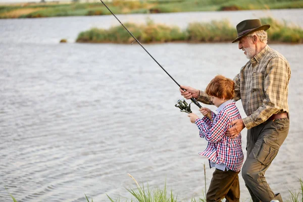 Bonito bom avô e neto puxando haste enquanto a pesca no fim de semana, vista lateral — Fotografia de Stock