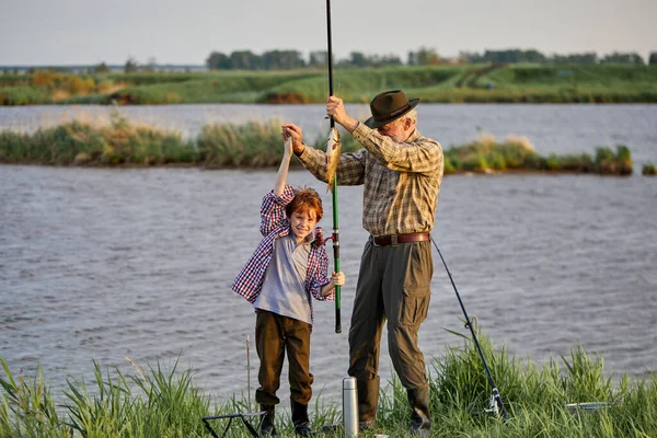 Pescador feliz con nieto mantenga pescado capturado. Pesca de éxito en el lago salvaje — Foto de Stock