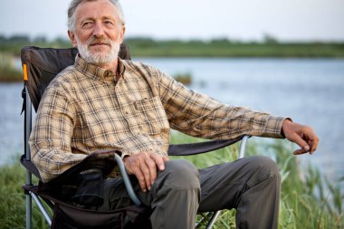 Hayalperest, kendine güvenen gri saçlı erkek gölün kenarındaki sandalyeye oturup poz veriyor.