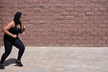 Spor elbiseli, koşan, koşan şişman bir kadının yan görüntüsü.