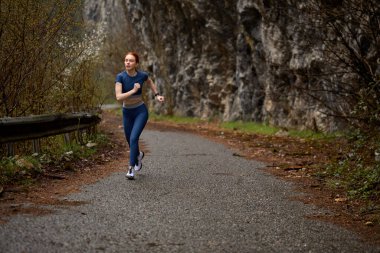 Aktif beyaz kadın, kızıl saçlı. Egzersiz yapıyor. Doğada tek başına koşuyor.