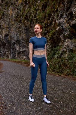 Çekici genç bayan fitness eğitmeni at kuyruğu ile mavi spor giyip dinleniyor.