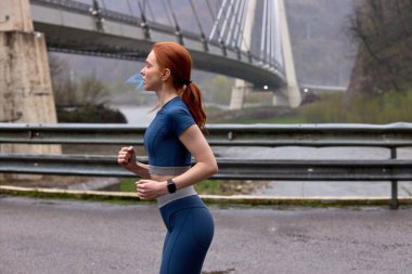 Köprüdeki kentsel alanda koşan beyaz giysili kadın.