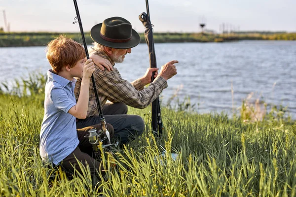 Abuelo y nieto van a pescar. Un poco de pesca ayudante. vista lateral, en el lago juntos — Foto de Stock