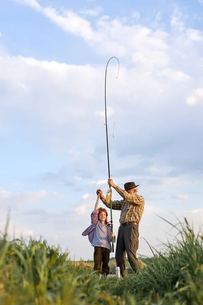Ragazzo caucasico in possesso di canna da pesca e pesce posa accanto al nonno la sera — Foto Stock