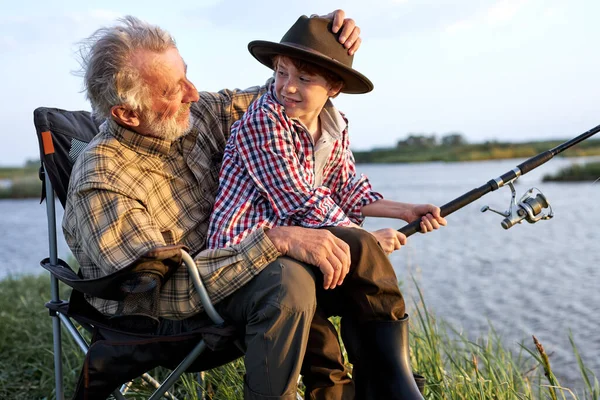 Abuelo enseñando nieto a pescar, le ayuda a sostener una caña, hablar — Foto de Stock