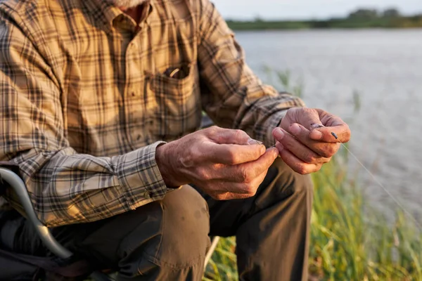 Maschio anziano ritagliato in camicia a scacchi mettere l'esca del verme sul gancio di canna da pesca — Foto Stock